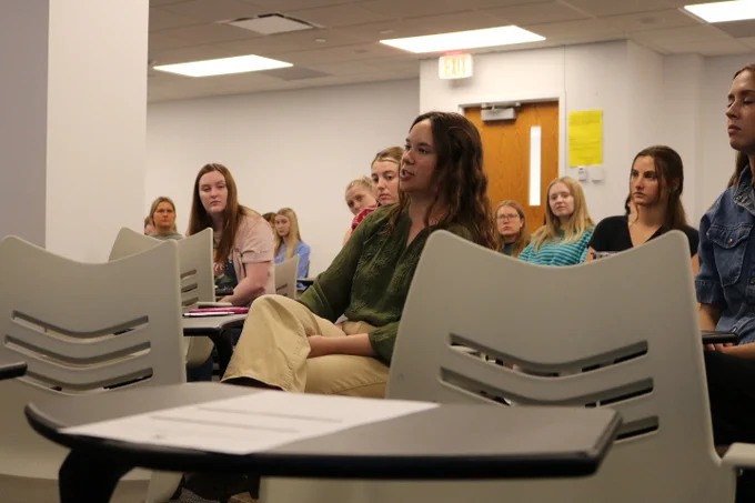 A female student asking a detailed question to Dr. Davis E. Henderson after his speech. In the background are more students listening intently.