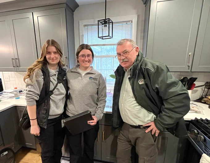 Three people smile for a photo together in a kitchen.
