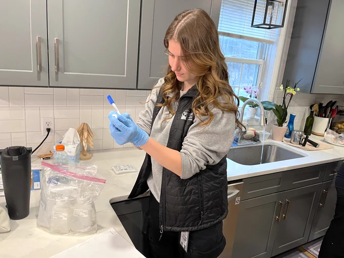 A woman wears latex gloves and labels a water sampling bottle.