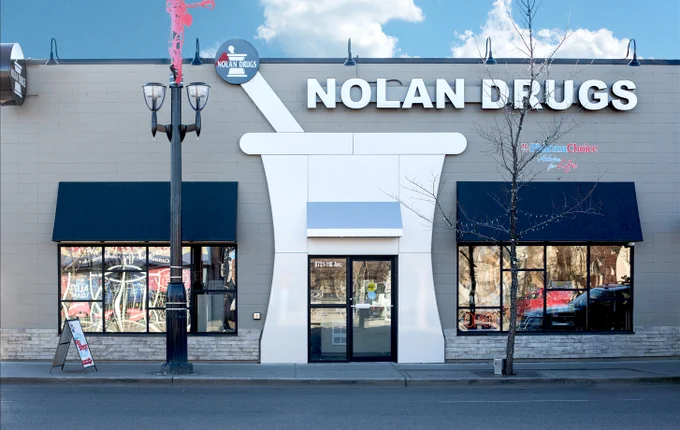 Front view of Nolan Drugs store with a large mortar and pestle design around the entrance and blue awnings over windows.