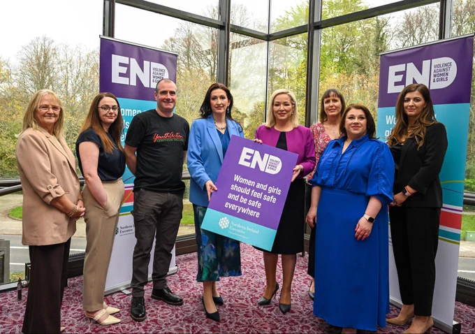 Image of eight people, two holding an Ending Violence Against Women and Girls (EVAWG) sign. The First Minister Michelle O'Neill and deputy First Minister Emma Little-Pengelly (centre) pictured with stakeholders at the launch of the second EVAWG Delivery Plan.