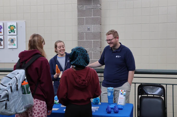 Woman and man talking with two high school students at Highlands Ranch Water's blue event booth in a high school hallway.