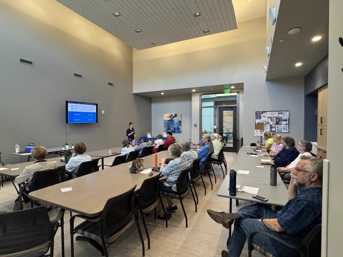 Large room with senior citizens sitting in chairs, facing the front of the room where a woman is speaking and hosting a trivia game at the Highlands Ranch Senior Center.