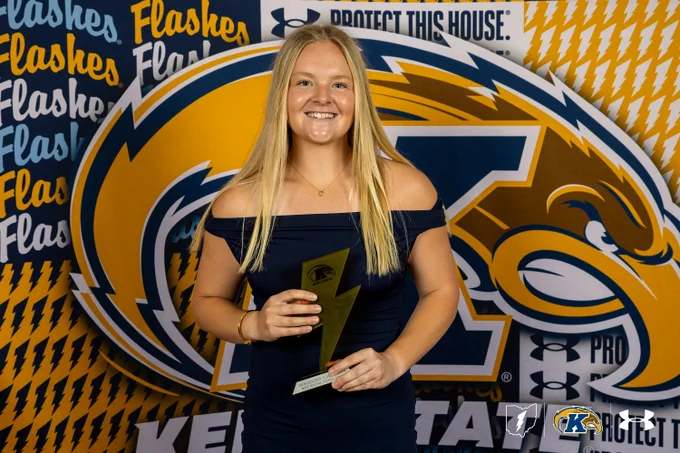 A Kent State student-athlete smiles while holding a golden lightning bolt-shaped award at the 2026 Golden Flashes Gala, posed in front of a Kent State Athletics step-and-repeat backdrop featuring the Golden Flashes logo and Under Armour branding. The award reads "2026 Golden Flashes Best Social Media Award.