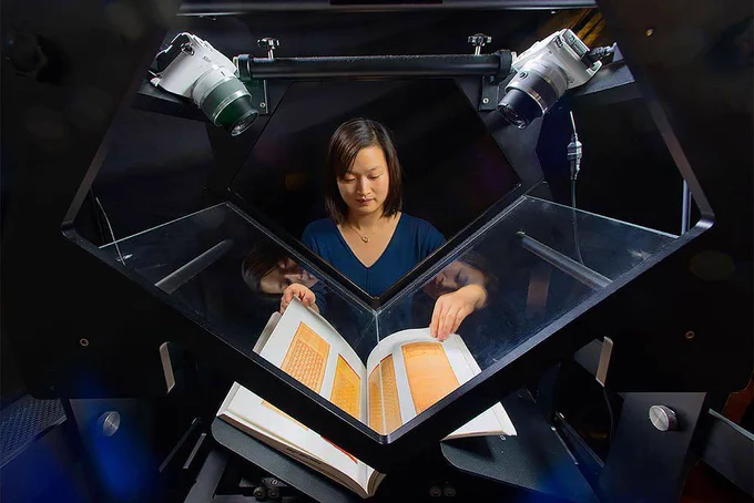 A person at the Internet Archive turning the pages of a book being digitized on a "scribe" station, which uses two cameras to shoot opposing pages simultaneously.