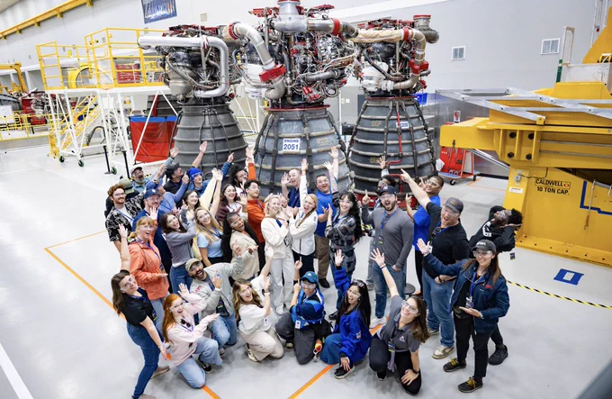 The NASA Social group poses for a funny photo as they point up at three engines that will be used for the Artemis 4 mission. Credit: NASA Stennis