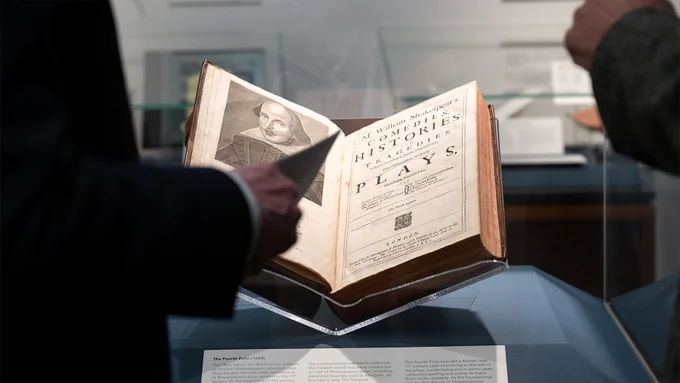 A close-up of an original Fourth Folio (1685), opened to its ornate title page and resting in a glass display case. The book is on loan from Sara Miller McCune for the Infinite Variety exhibition.