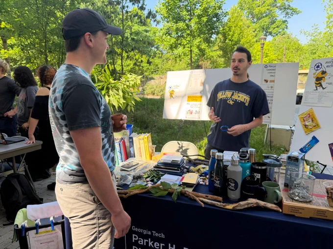 Two people talk at a Georgia Tech outreach table displaying reusable items and recycling information boards.