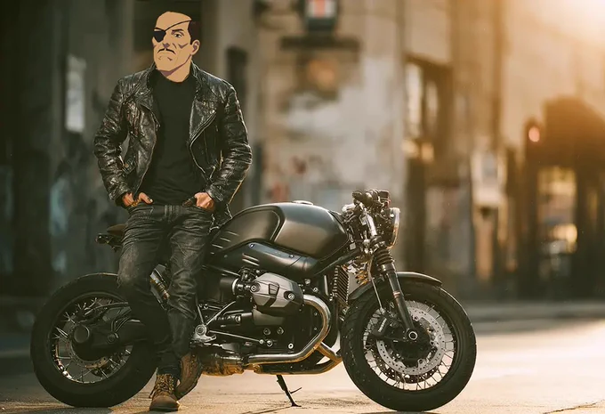 Kregg, dressed in dark jeans and a black leather jacket leans against a motorcycle