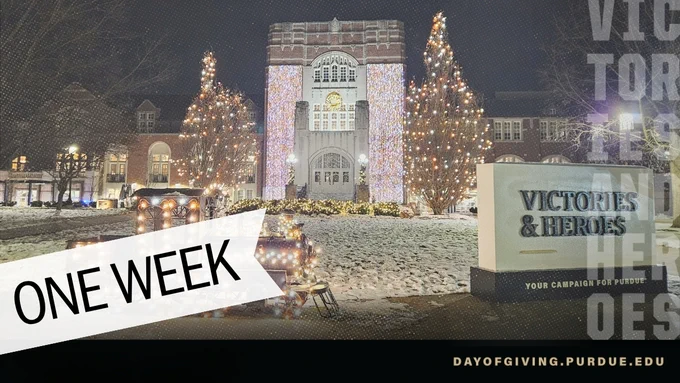 Purdue Memorial Union snow covered front lawn and light display in the dark featuring lit up train and Victories & Heroes campaign sign.