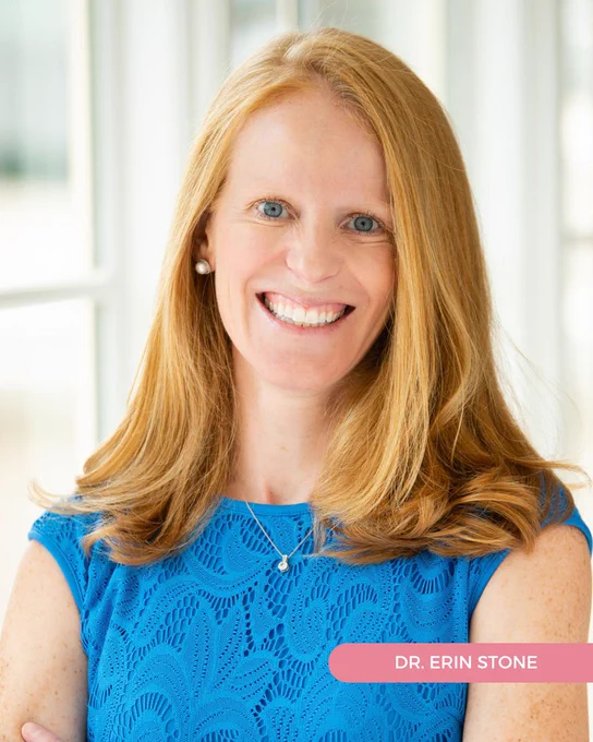 Dr. Erin Stone of Tryon Women's Center wears a blue dress and smiles in a professional portrait in front of a paned glass window