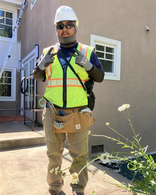 A Sonic field service technician standing in front of a Sonic member's home, throwing up two peace signs.