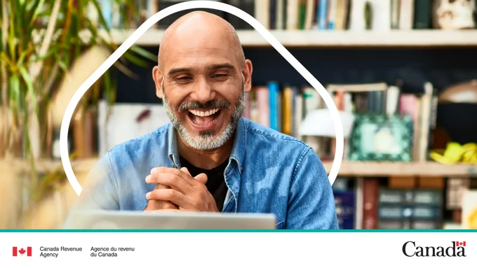 A person laughs and clasps their hands while looking at a computer screen.