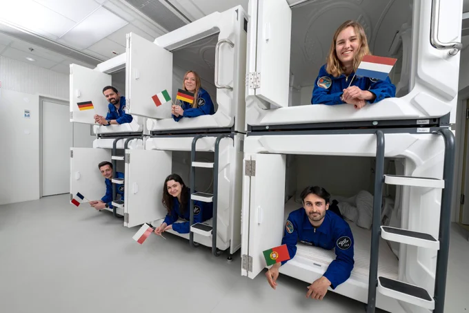 Participants in the SOLIS100 isolation study in their sleeping pods holding the flags of their home countries. The six volunteers will live and work in isolation for the full 100 days, following structured daily schedules and operational constraints similar to those of a space mission.