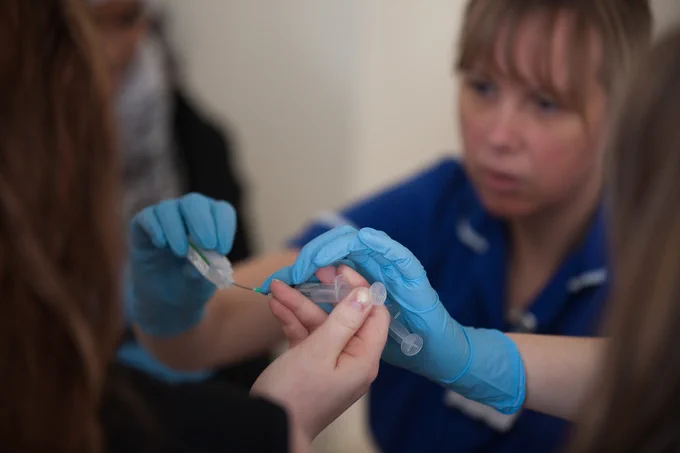 A nurse wears gloves and holds a needle.