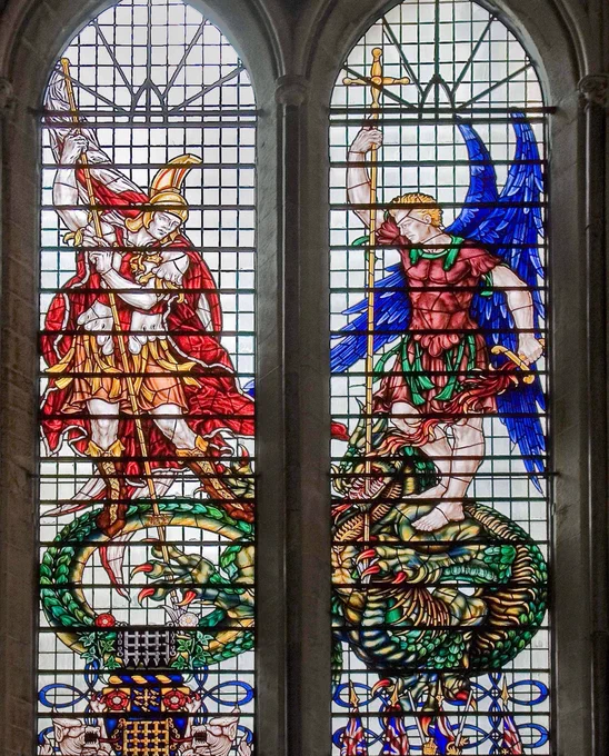 A large stained glass window showing St Michael - depicted wearing gold armour and a red cloak and holding a flaming sword - and St George - who has large blue wings - slaying a fearsome-looking green and gold dragon.