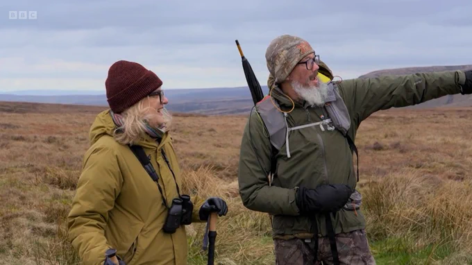 BBC Countryfile presenter Charlotte Smith and Natural England species ecologist Dr Carlos Bedson stood in front of a moorland landscape. Carlos is pointing to something in the distance.