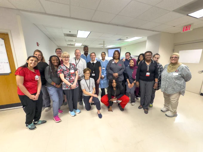 Group photo of diverse healthcare workers and staff posing together in a hospital hallway.