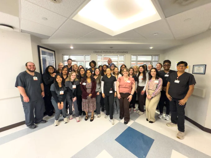 Group photo of diverse medical professionals and students standing together in a clinical hallway under a sign reading 'Clinical Simulation Laboratory'.