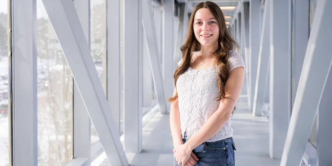 Michigan Tech student Ashley Baird stands smiling at the camera in the walkway between the Michigan Tech Van Pelt and Opie Library and Rekhi Builidng. 