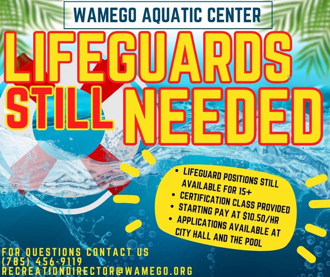 Bright, colorful hiring poster for the Wamego Aquatic Center featuring a water background with splashes and a large life preserver. Bold yellow and red text reads “Lifeguards Still Needed.” A yellow bubble lists details: lifeguard positions available for ages 15 , certification class provided, starting pay at $10.50 per hour, and applications available at City Hall and the pool. Contact information at the bottom includes phone number (785) 456-9119 and email recreationdirector@wamego.org