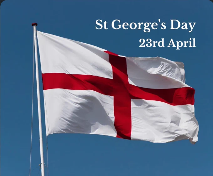 The Flag of England (St George's Cross) waving against a clear blue sky, with white text in the upper right reading "St George's Day 23rd April".