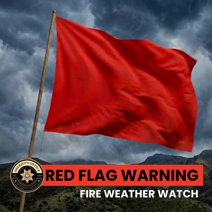 Graphic showing a large red warning flag waving on a pole against dark storm clouds and a mountain landscape. At the bottom left is the Jefferson County Sheriff’s Office logo. Bold text across the image reads, “RED FLAG WARNING” and “FIRE WEATHER WATCH.”