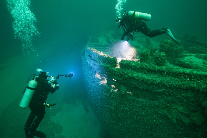 Two scuba divers explore an underwater shipwreck.