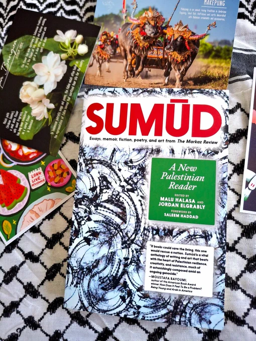 A photograph of a book titled Sumud: Essays, Memoir, Fiction, Poetry, and Art from The Markaz Review. The book title is printed in red, and the cover has swirling forms of barbed wire. The book is placed on a keffiyeh.