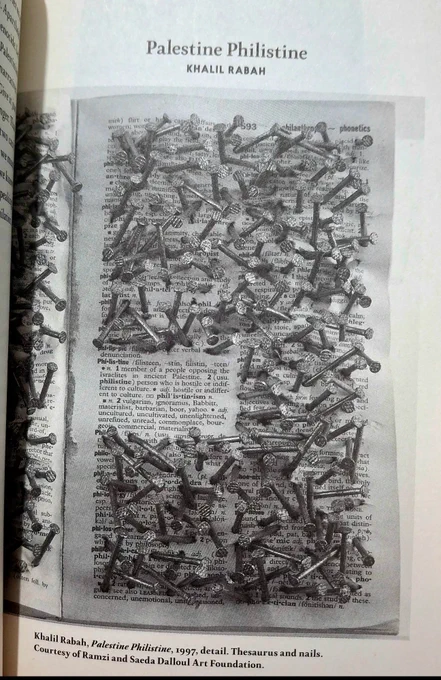A page from Sumud book featuring a full page image of details from Palestine Philistine, an installation by Khalil Rabah. It showcases an open page in Oxford Desk Dictionary and Thesaurus. Masonry nails were hammered around the word philistine and its descriptions. 