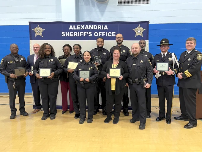 Sworn and civilian Alexandria Sheriff's Office employees holding plaques and smiling at an awards ceremony