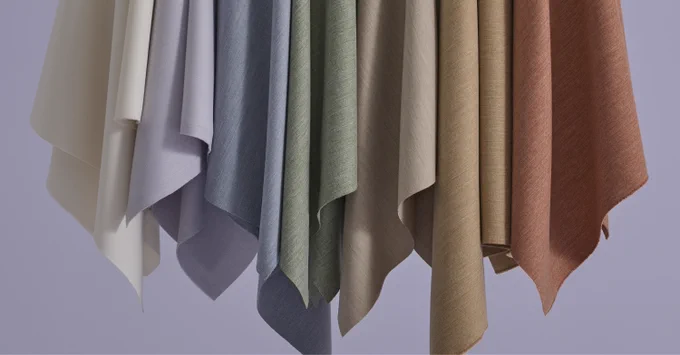 Close-up of hanging fabric swatches in soft neutral tones including white, gray, green, beige, and brown against a light background.