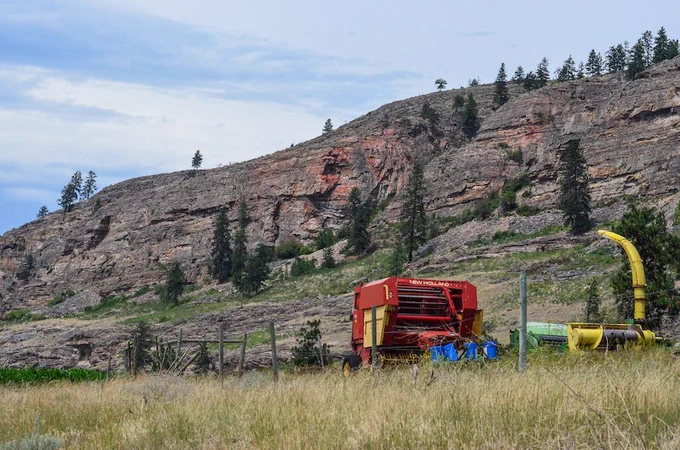 Landscape photo with farm equipment in foreground and the Vaseux Cliffs in the background.