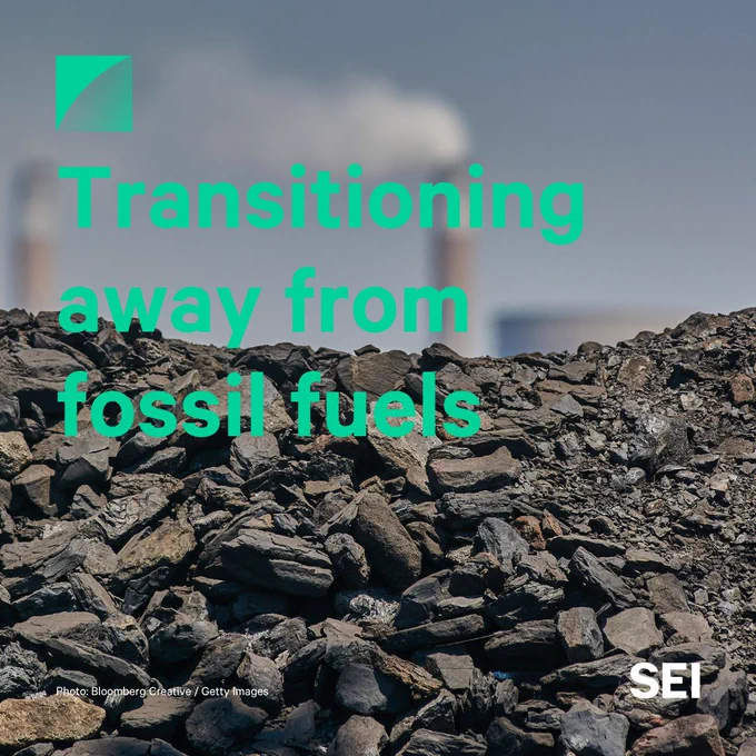 Photo of a coal pile in front of smoke stacks with green text reading, "Transitioning away from fossil fuels"
