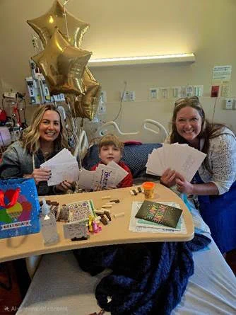 Henry Jones and two adults smile and pose for a picture while holding birthday cards.