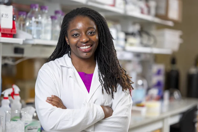 Professor Erika Moore standing in her lab, smiling at the camera while wearing a white lab coat.