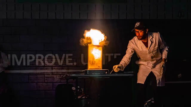 A person wearing a lab coat and hat igniting a contraption in the dark
