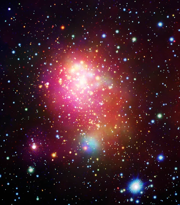 This is a multiwavelength image of the Westerlund 1 star cluster and the surrounding region in X-ray and optical light. The black canvas of space is peppered with colored dots of light of various sizes, mostly in shades of red, green, blue, and white.

At the center of the image is a hazy cloud of red and yellow gas encircling a grouping of tightly packed gold stars. The arrangement and distribution of stars in the cluster call to mind effervescent soda bubbles dancing above the ice cubes of a recently poured beverage.