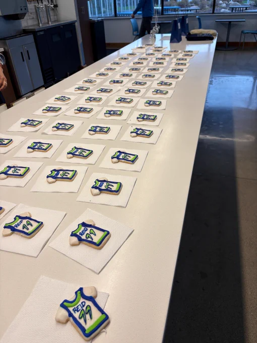 Decorated cookies shaped like basketball jerseys with the word "FEED" and the number "99" are arranged in rows on a long white table. Each cookie is placed on a napkin.