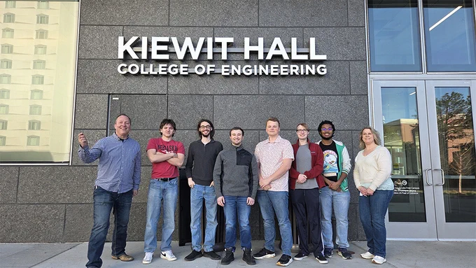 Eight people — six Husker students and two professors — stand outside Kiewit Hall.