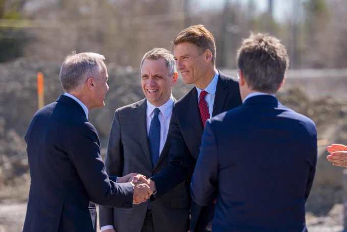 Two people smiling and shaking hands. Another person smiling alongside and another onlooker. 