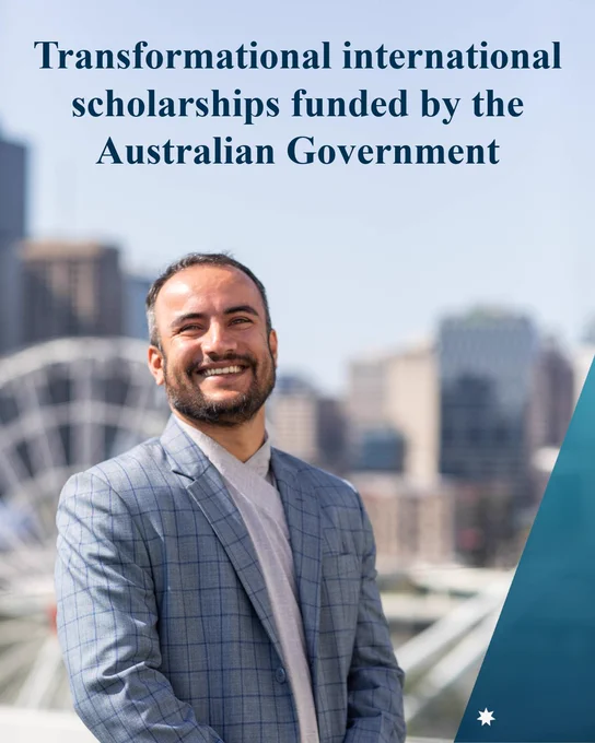 A man stands smiling wearing a suit jacket with Luna Park Sydney in the background with text: Transformational international scholarships funded by the Australian Government 
