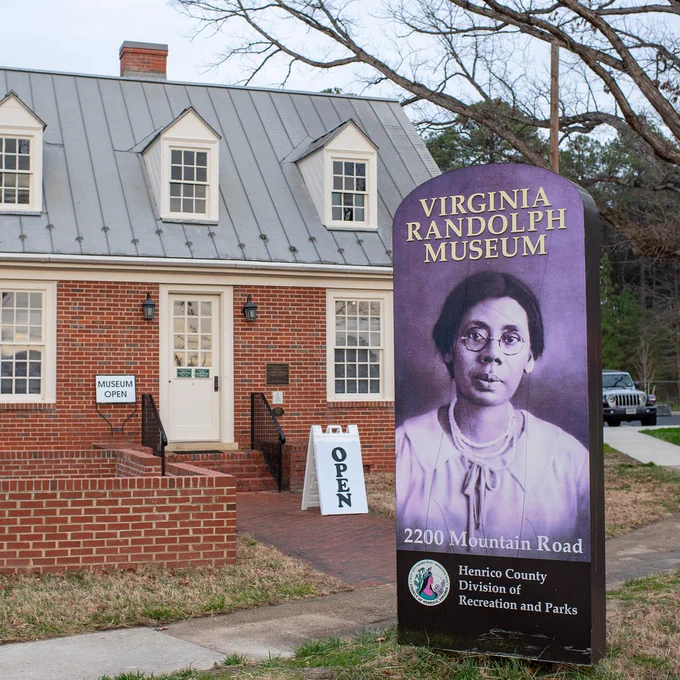 Brick building with sign for Virginia Randolph Museum, featuring a portrait of a woman in glasses against a purple background.