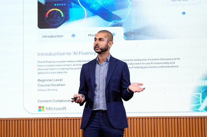 Speaker presenting AI Fluency course on stage with Microsoft slide behind.