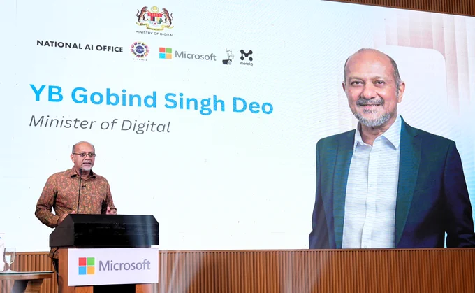 Speaker at podium during Microsoft event with large screen showing minister title.