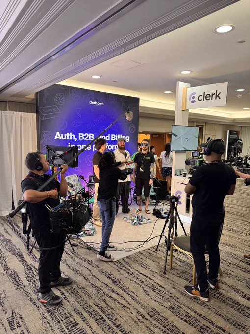 Jason Lengstorf standing with Robbie Wagner and Adam Argyle in the Clerk booth at React Miami, surrounded by a camera crew