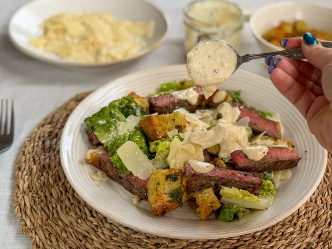 PGI Welsh Beef steak Caesar salad - the photo shows me drizzling the Caesar dressing over the plated salad. 