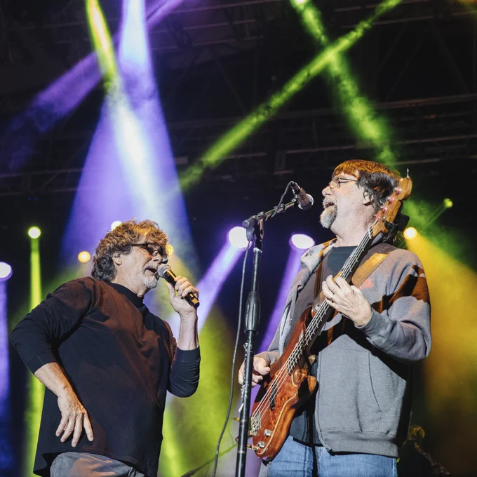 The singer and Bass player for the popular band, Alabama, sincing on stage with green and purple lights in the background. 
