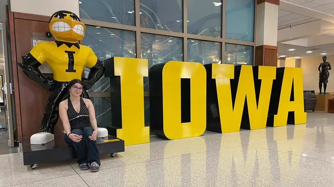 Student sitting in front of statue Herky and "IOWA."

