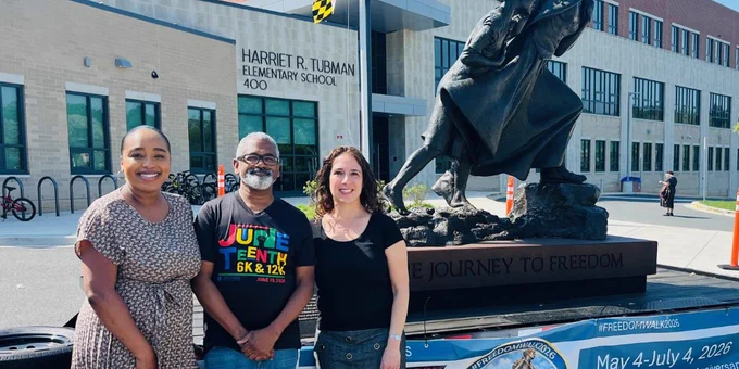 Three people, including Anthony Cohen, stand in front of a Harriet Tubman Elementary School statue depicting her leading a child to freedom.